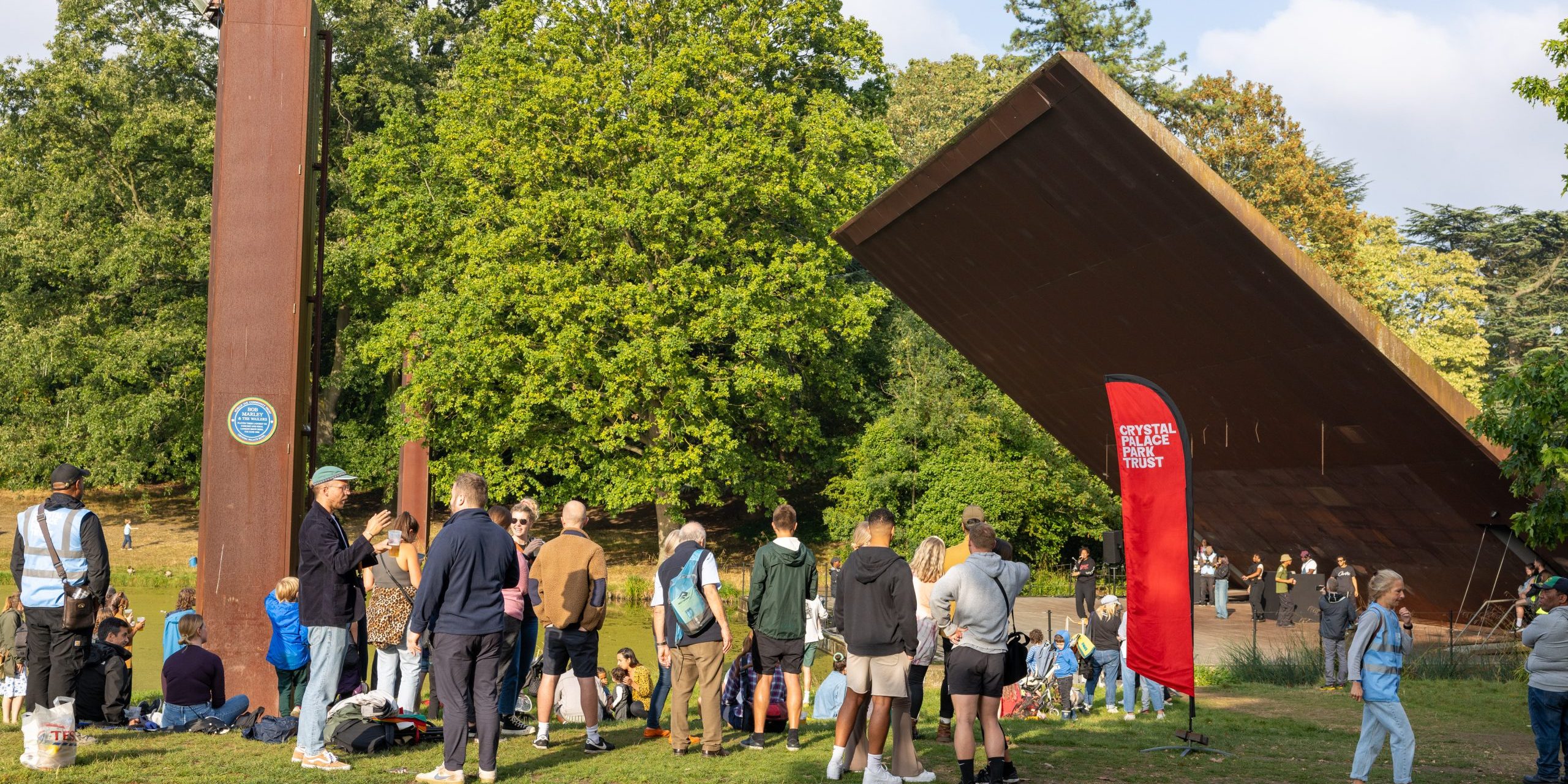CPPT_Handover_Festival (157 of 164) A group of over 20 people of a range of ages stood and sat by the Concert Platform in Crystal Palace Park at a party to celebrate the handover of the park to the Crystal Palace Park Trust.